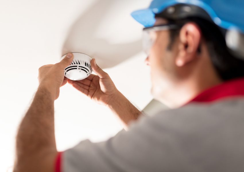 person in a blue hard hat fixing a smoke detector